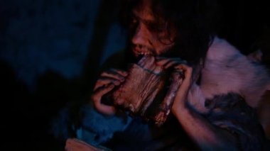 Neandertal veya Homo Sapiens Aile Pişirme Hayvan Eti Bonfire üzerinde ve sonra yeme. Prehistorik Avcı-Toplayıcılar Kabilesi Gece Karanlık Korkunç Mağarada Yemek Hayvan Derileri Giyen. Yakın Çekim
