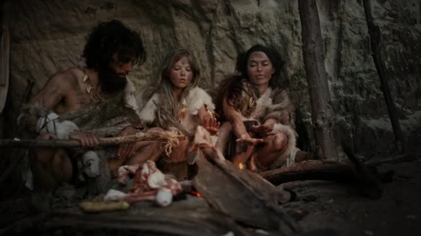 Tarih öncesi avcı-toplayıcı kabilesi Hayvan Derisi Giyen Gece Bir Mağarada Yaşıyor. Neanderthal ya da Homo Sapiens Ailesi Şenlik Ateşi 'nde Isınmaya Çalışıyor, Ateşin Üzerinde Elele tutuşuyor, Yemek Pişiriyor — Stok video