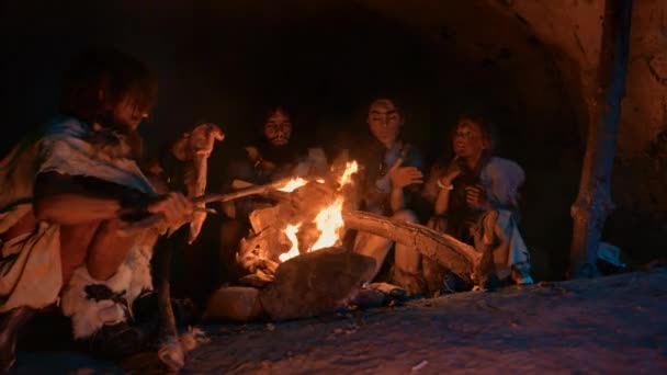 Famille Neandertal ou Homo Sapiens Cuire de la viande animale sur le feu de joie, puis la manger. Tribu de chasseurs-cueilleurs préhistoriques portant des peaux d'animaux mangeant dans une grotte sombre et effrayante la nuit — Video