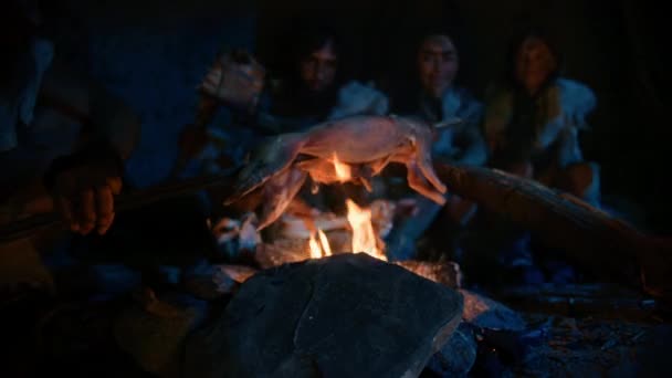 Neanderthal or Homo Sapiens Family Cooking Animal Meat over Bonfire and then Eating it. Tribe of Prehistoric Hunter-Gatherers Wearing Animal Skins Eating in a Dark Scary Cave at Night. Close-up Shot — Stock Video