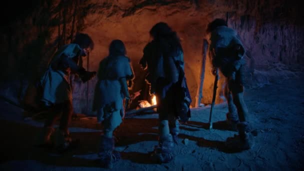 Plemię prehistorycznych łowców-zbieraczy noszących skórki zwierząt żyją w jaskini nocą. Neandertalczyk lub homo sapiens rodzina stara się ogrzać w ognisku, trzymając ręce nad ogniem. Po widoku wstecz — Wideo stockowe