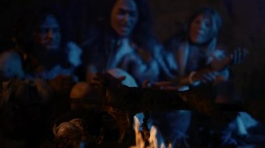 Neandertal ya da Homo Sapiens Ailesi Şenlik Ateşi Üzerinde Hayvan Eti Pişiriyor ve Sonra Onu Yiyor. Tarih Öncesi Avcı-Toplayıcılar kabilesi Hayvan Derisi Izgara Giyiyor ve Geceleri Mağarada Et Yiyiyor