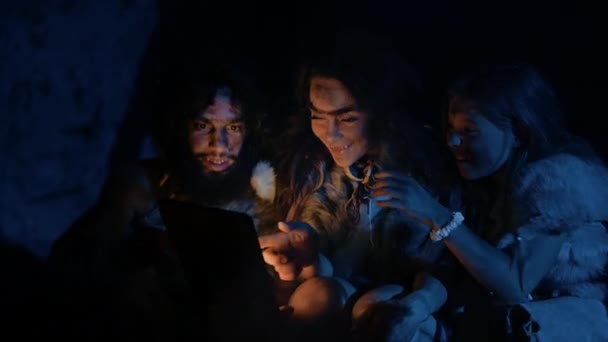 Tribu des chasseurs-cueilleurs préhistoriques et primitifs portant des peaux d'animaux Utilisez un ordinateur tablette numérique dans une grotte la nuit. Neandertal ou Homo Sapiens Family Navigation sur Internet, Regarder des vidéos, Séries TV — Video