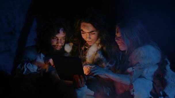 Tribù di preistorici, cacciatori-raccoglitori primitivi che indossano pelli di animali utilizzano computer tablet digitale in una grotta di notte. Neanderthal o Homo Sapiens Famiglia Navigazione Internet, Guardare video, Streaming — Video Stock