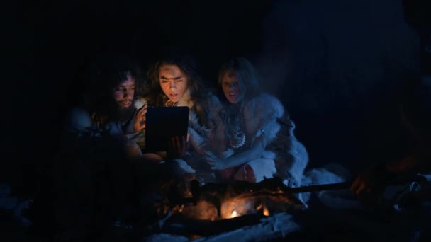 Tribe of Prehistoric, Primitive Hunter-Gatherers Wearing Animal Skins Use Digital Tablet Computer em uma caverna à noite. Neanderthal ou Homo Sapiens Família Navegação Internet, Assistir Vídeos, Transmissão — Vídeo de Stock