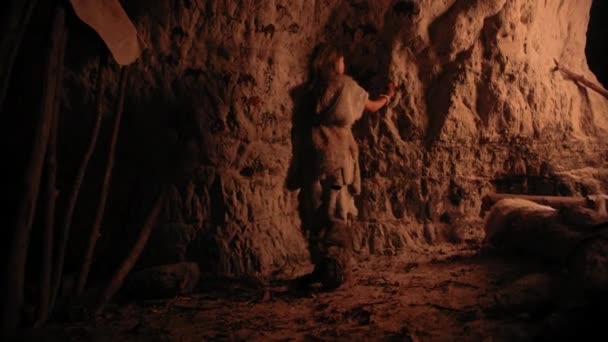 Un enfant primitif néandertalien préhistorique portant une peau d'animal dessine des animaux et des résumés sur les murs la nuit. Création de la première grotte d'art avec des pétroglyphes, peintures rupestres éclairées par le feu. Vue arrière — Video