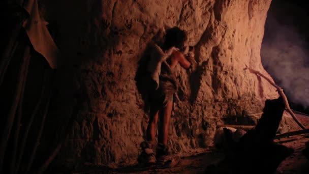 Pré-histórico primitivo Neandertal vestindo pele de animal desenha animais e resumos nas paredes à noite. Criando Primeira Caverna Arte com Petroglifos, Pinturas Rochosas Iluminadas pelo Fogo. Visão traseira — Vídeo de Stock