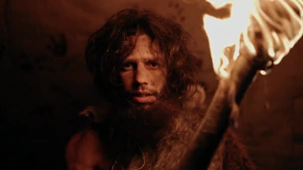 Portret pierwotnego jaskiniowca noszącego skórę zwierzęcia stojącego nocą w jaskini, trzymającego pochodnię z ogniem. Prymitywny łowca neandertalczyków / Homo Sapiens w nocy sam w swojej komorze — Wideo stockowe