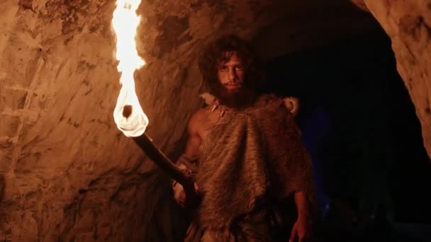 Portrét pravěkého jeskynního muže s kůží zvířete, který v noci zkoumá jeskyni, drží pochodeň s ohněm a dívá se na kresby na stěnách v noci. Neandrtálské hledání bezpečného místa pro strávení noci — Stock video