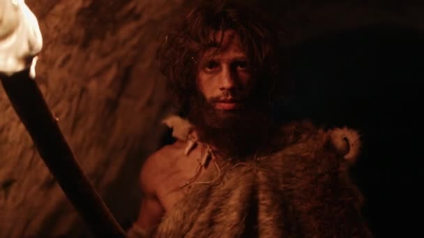 Porträt eines Höhlenmenschen mit tierischer Haut, der nachts die Höhle erkundet und dabei eine Fackel mit Feuer hält, während er nachts Zeichnungen an den Wänden betrachtet. Neandertaler auf der Suche nach sicherem Übernachtungsplatz