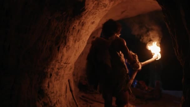 Primeval Caveman noszenia Animal skóry odkrywania jaskini w nocy, trzymając Torch z ogniem patrząc na rysunki na ścianach w nocy neandertalczyków wyszukiwanie bezpieczne miejsce do spędzenia nocy. Widok wstecz po — Wideo stockowe