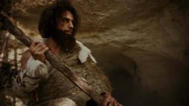 Hayvan Derisi Giyen Primeval Caveman Tutar Stone Hammer Prehistorik Orman Etrafında Görünüyor, Hayvan Av Hunt hazır. Neandertal Ormana Avlanmaya Gidiyor. Dramatik Düşük Açılı Yay Çekimi