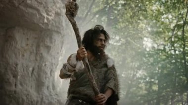 Hayvan Derisi Giyen Primeval Caveman Taş Uçlu Çekiç Tutar Mağara dan çıkar ve Prehistorik Manzara Etrafında Bakar, Hayvan Prey Hunt hazır. Neandertal Ormana Avcılık Going