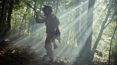 Tarih öncesi ormanda Hayvan Derisi Giyen İlkel Mağara Adamı 'nın Portresi ve Taş Ucu Mızrakla Kürk Avı. İlkel Neandertal Avcısı Ormana Mızrak Atmaya Hazır