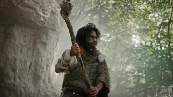 Primeval Caveman Wearing Animal Skin Holds Stone Tipped Hammer Comes out of the Cave and Looks Around Prehistoric Landscape, Ready to Hunt Animal Prey. Neanderthal Going Hunting into the Jungle — Stock Video