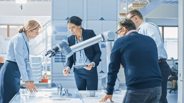 Equipe diversa de engenheiros de robótica industrial reunidos em torno da mesa com o braço do robô, eles manipulam e programam para pegar e mover componentes metálicos . — Fotografia de Stock