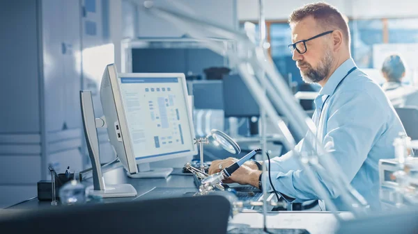 Ingénieur en développement électronique travaillant sur l'ordinateur, la conception de la carte mère, l'entretien des appareils et les cartes de circuits de soudure. Professionnel travaillant dans un bureau lumineux et moderne — Photo