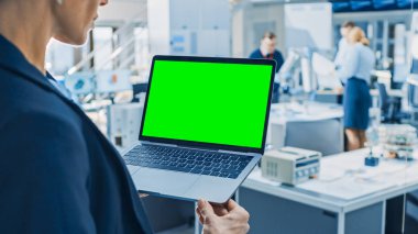 Mühendis Yeşil Mock-up Ekran Laptop Bilgisayar tutar. Modern Parlak Araştırma Tesisinde Fonksiyonel Robot Kolu ile Çalışan Endüstri Mühendislerinden Oluşan Arka Plan Ekibinde