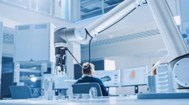 Modern Robot Kolu Programlı Olarak Metal Bileşeni Alır, Kaldırır ve Hareket Ettirir. Mühendislik Tesisinde Yazılım, Programlama ve Makine Öğrenimi Üzerine Çalışan Endüstriyel Robotik Mühendisleri