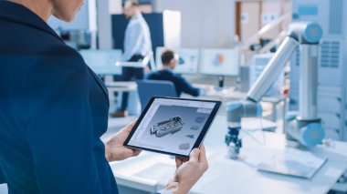 Şık Kadın Endüstriyel Robotik Mühendisi Cad Yazılımı ile Tablet Bilgisayar kullanır ve Manipüle ve Program Robot Kolu Kaldırma için, Hareketli Nesneler. Bulut Bilişim için Teknoloji Araştırma Tesisi