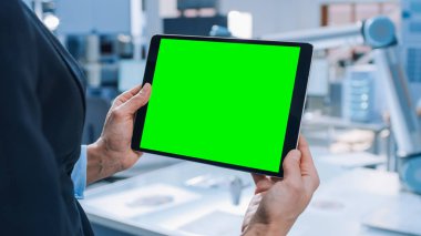 Mühendis Yeşil Mock-up Ekran Dijital Tablet Bilgisayar tutar. Modern Parlak Araştırma Tesisinde Fonksiyonel Robot Kolu ile Çalışan Endüstri Mühendislerinden Oluşan Arka Plan Ekibinde