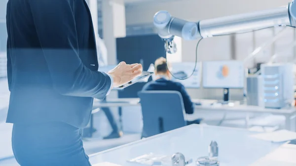 Elegante ingegnere robotica industriale femminile utilizza computer tablet con software CAD e per manipolare e programmare braccio robot per il sollevamento, oggetti in movimento. Strumento di ricerca tecnologica per il cloud computing — Foto Stock