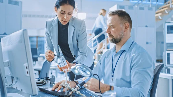 Kadın Endüstri Mühendisi Elektronik Uzmanı ile Konuşuyor, Metal Komponent Prototipini Tutuyor, Bilgisayarda Çalışıyor. Şık İnsanlarla Modern ve Parlak Ofis