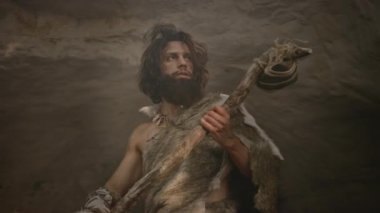 Hayvan Derisi Giyen Primeval Caveman Taş Çekiç Tutar Mağara çıkar ve Prehistorik Manzara Etrafında Görünüyor, Hayvan Prey Hunt hazır. Neandertal Ormana Avlanmaya Gidiyor. Düşük Açılı Yay Çekimi