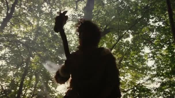 La silhouette de l'homme des cavernes primitif portant la peau animale tient le marteau de pierre regarde autour de la forêt préhistorique, prêt à chasser la proie animale. Neanderthal Going Hunting into the Jungle. Dramatique tir à l'arc à faible angle — Video
