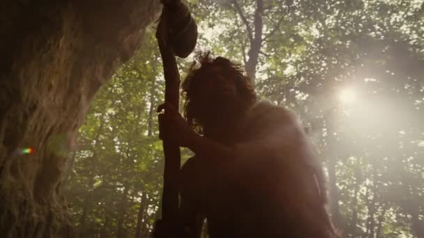 Silhueta de Caveman Primeval vestindo pele animal detém pedra martelo olha em torno da floresta pré-histórica, pronto para caçar presas animais. Neandertal vai caçar na selva. Arco de ângulo baixo dramático tiro — Vídeo de Stock