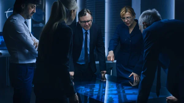 Diverse Team of Government Intelligence Agents Standing Around Digital Touch Screen Table and Tracking Suspect, Senior Officer does Interactive Gesturing. Big Dark Surveillance Room. — Stock Photo, Image