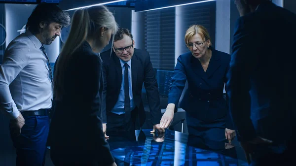 Diverse Team of Government Intelligence Agents standing Around Digital Touch Screen Table and Tracking Suspect, senior officer does Interactive Gesturing. Big Dark Surveillance Room. — Stock fotografie