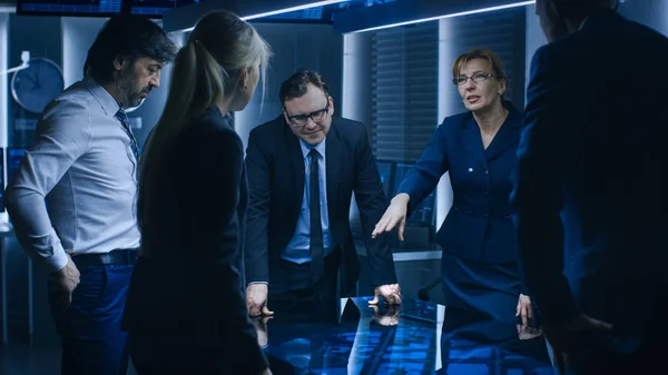 Diverse Team of Government Intelligence Agents Standing Around Digital Touch Screen Table and Tracking Suspect, Senior Officer does Interactive Gesturing. Big Dark Surveillance Room. — Stock Photo, Image