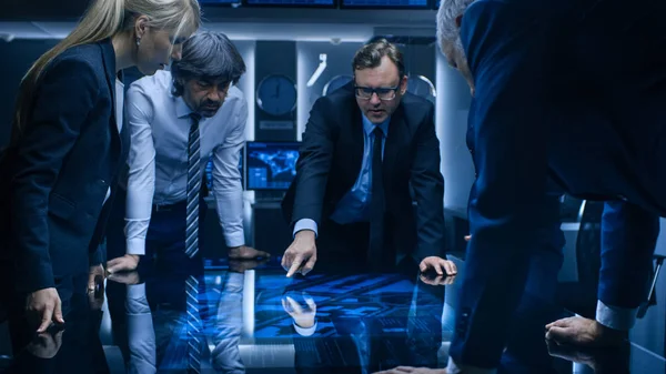 Equipe Diversa de Agentes de Inteligência do Governo em pé em torno da mesa de tela táctil digital e rastreando suspeitos. Grande sala de vigilância escura cheia de telas de computador. — Fotografia de Stock