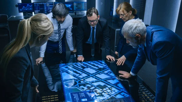 High Angle Shot of Team of Government Intelligence Agents Talking while Standing Around Digital Touch Screen Table and Tracking Suspect. Satellite Surveillance Operation in the Monitoring Room. — Stock Photo, Image