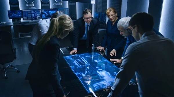 Team van de overheid Intelligentie / FBI-agenten staan rond Digital Touch Screen Table en het bijhouden van verdachte voertuig met behulp van satellietbewaking in de monitoringkamer. — Stockfoto