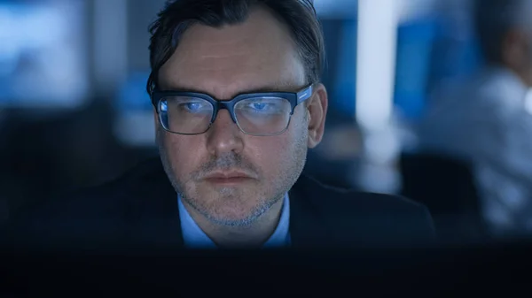Portrét hezkého experta na nošení brýlí na počítači. V pozadí aktivní odborníci. — Stock fotografie