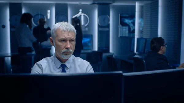 Retrato do Especialista Sênior Preocupado Trabalhando em Computador na Sala de Controle de Monitoramento com Equipes Solucionando Problemas em segundo plano. — Fotografia de Stock