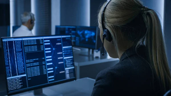 Vista posteriore del controller femminile con auricolare che lavora sul personal computer, processi di monitoraggio nella sala di controllo del sistema piena di agenti di intelligence speciali. — Foto Stock