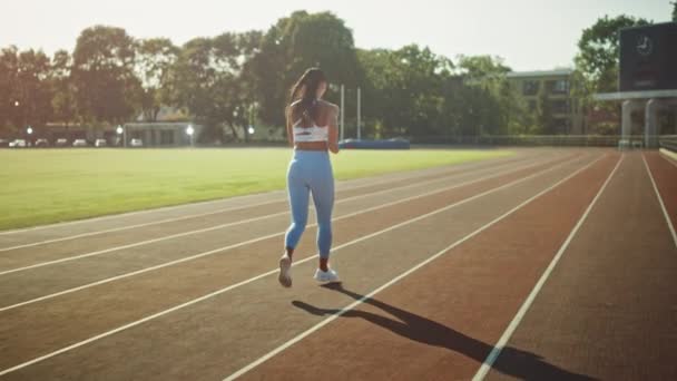 美丽的健身女孩在浅蓝色运动上衣和在体育场慢跑。她在一个温暖的夏日午后跑步。运动员在跑道上进行日常体育锻炼。慢动作. — 图库视频影像