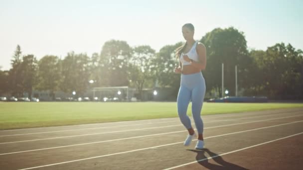 Девушка в светло-синем спортивном топе и бегает по стадиону. Она бежит теплым летним днем. Спортсмен, практикующий рутинный спорт на треке. Slow Motion . — стоковое видео