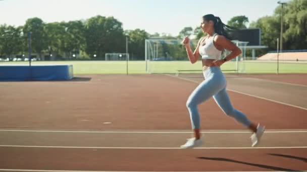 Belle femme de fitness en haut athlétique bleu clair et leggings Jogging dans le stade. Elle court vite un après-midi d'été chaud. Athlète faisant sa pratique sportive de routine. Tir de suivi . — Video