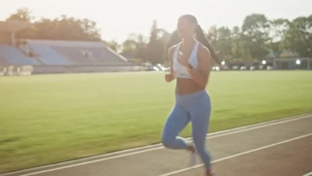 Mujer feliz y sonriente de fitness con top atlético azul claro y polainas corriendo en el estadio. Ella está corriendo rápido en un cálido día de verano. Atleta haciendo su práctica deportiva. Tracking Shot . — Vídeo de stock