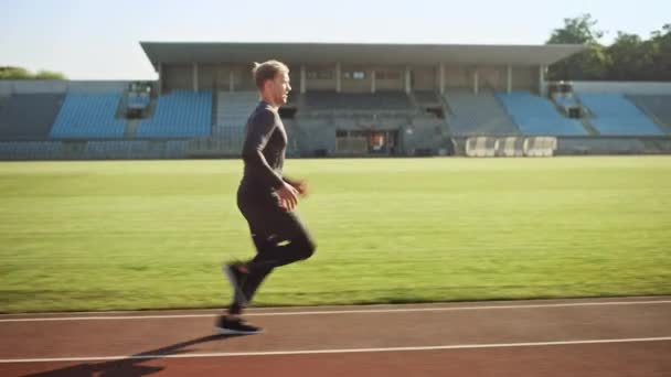 경기장에서 회색 셔츠와 반바지 조깅에 운동 적합 남자. 그는 따뜻한 여름 오후에 빨리 달리고 있습니다. 그의 일상적인 스포츠 연습을 하 고 선수. 트래킹 샷. — 비디오