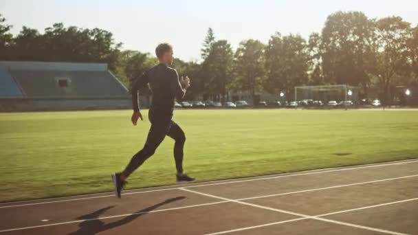 경기장에서 회색 셔츠와 반바지 조깅에 운동 적합 남자. 그는 따뜻한 여름 오후에 빨리 달리고 있습니다. 그의 일상적인 스포츠 연습을 하 고 선수. 슬로우 모션 트래킹 샷. — 비디오
