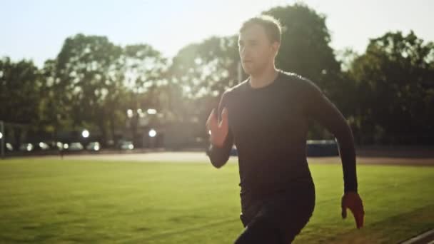 Спортивна людина Fit в сіру сорочку і шорти біг на стадіоні. Він швидко біжить на теплий літній день. Спортсмен робить свою рутинну спортивну практику. Повільне відстеження руху постріл. — стокове відео
