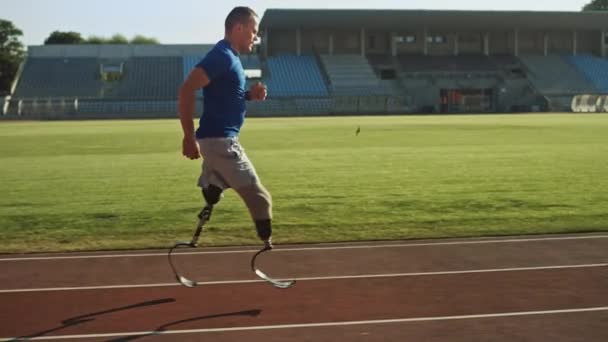 Atletisk funktionshindrade Fit man med protetiska löpar knivar är träning på en utomhus stadion på en solig eftermiddag. Amputerad löpare jogging på en Stadionbana. Motiverande Sportbilder. Spårnings bild. — Stockvideo