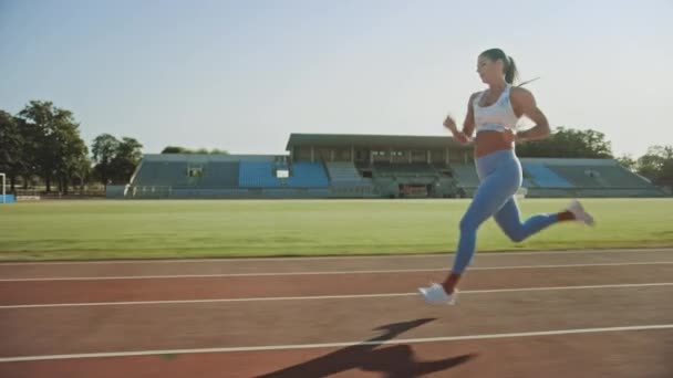 Beautiful Fitness Woman in Light Blue Athletic Top and Leggings Jogging in a Stadium. She is Running on a Warm Summer Afternoon. Athlete Doing Her Routine Sports Practice on a Track. Slow Motion. — Stock Video