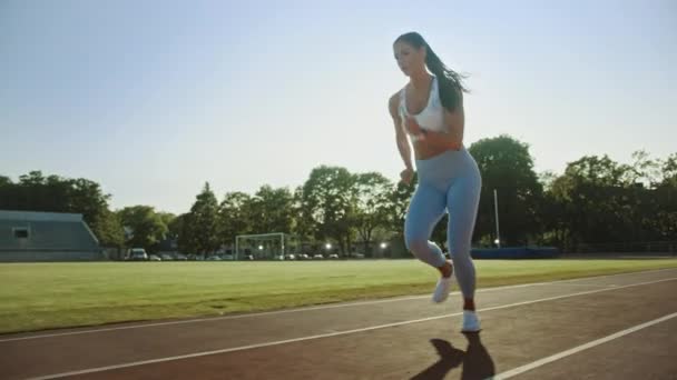 Mooie fitness vrouw in licht blauwe atletische top en legging begint een sprint run in een openlucht stadion. Ze loopt op een warme zomerdag. Atleet doet haar sportbeoefening. Tracking shot. — Stockvideo