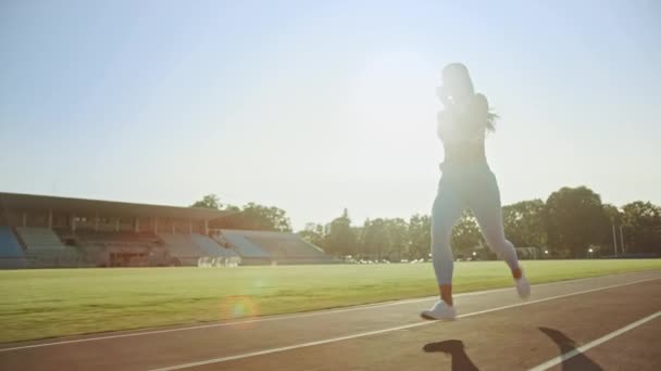 Mooie fitness vrouw in licht blauwe atletische top en legging joggen in een stadion. Ze loopt op een warme Zomermiddag. Atleet doet haar routine sportpraktijk op een spoor. Slow Motion. — Stockvideo